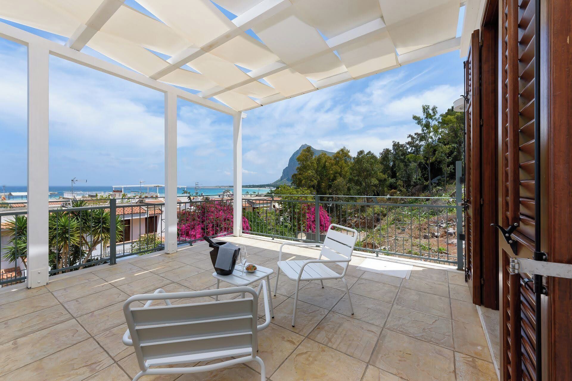 A balcony with a white chair and table, overlooking a scenic view of the sea and a mountain.
