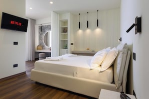 A modern hotel room with a large bed, a flat-screen TV mounted on the wall, a built-in shelf with decorative items, and a window with curtains. - Albergo Auralba (San Vito Lo Capo)