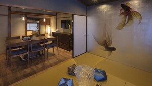 A traditional Japanese room with tatami flooring, a low table with chairs, and a wall with a fish painting.
