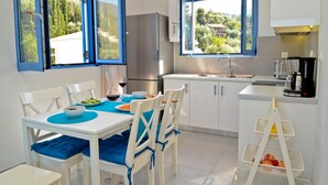 A modern kitchen with white cabinets, a stainless steel refrigerator, a sink, and a window with a view of greenery.