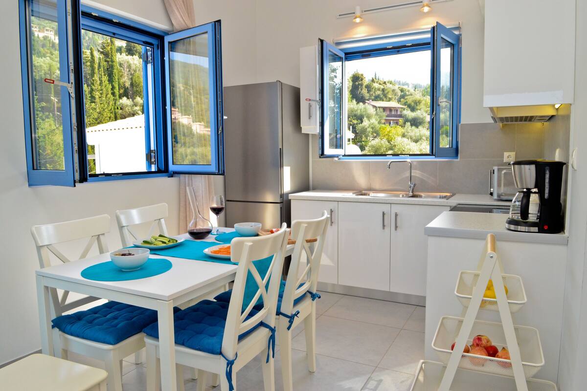 A modern kitchen with white cabinets, a stainless steel refrigerator, a sink, and a window with a view of greenery.