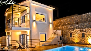 A modern two-story building with a swimming pool, outdoor seating, and a stone wall.