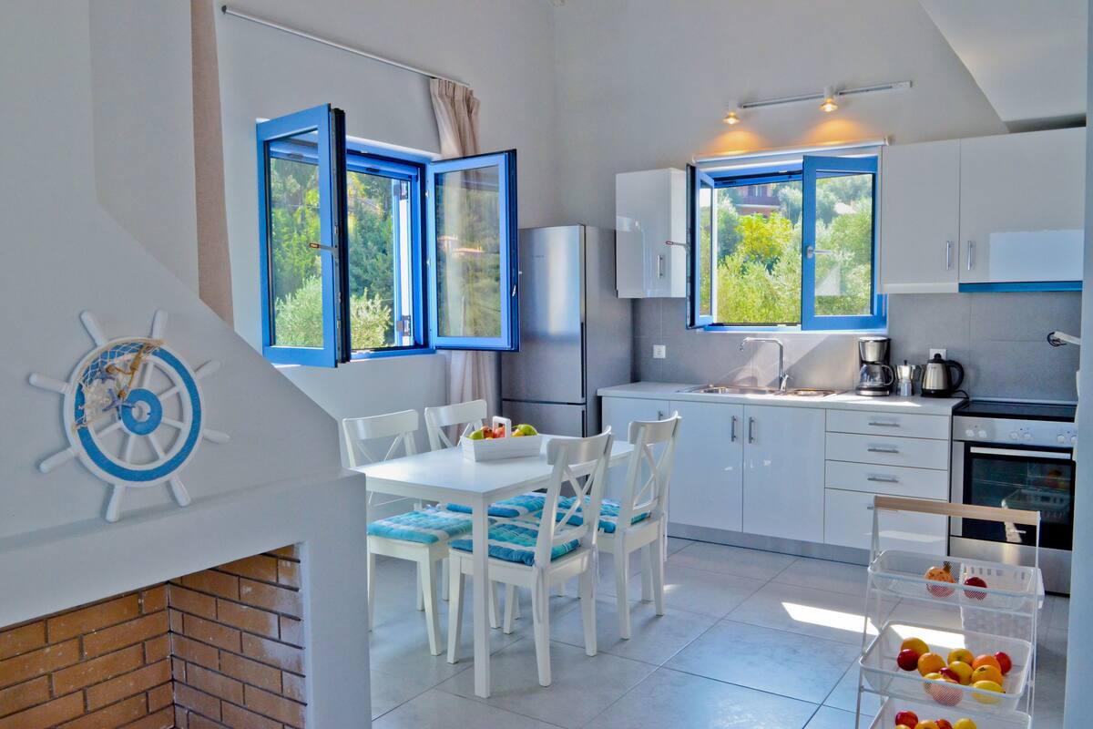 A modern kitchen with white cabinets, a dining table with blue cushions, and a brick fireplace.