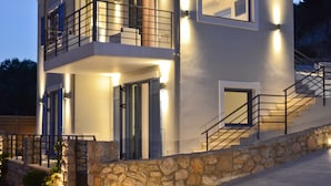 A modern two-story house with a stone facade, a balcony, and a staircase leading to the upper floor.
