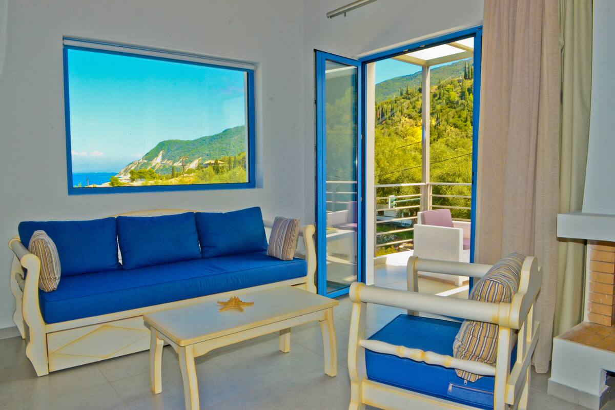 A room with a blue sofa, a small table, and a chair with a view of the outdoors.