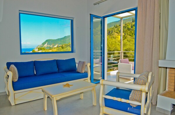 Una habitación con un sofá azul, una mesita y una silla con vistas al exterior.