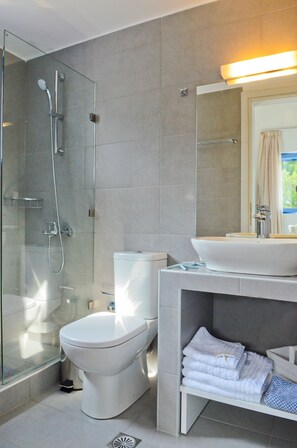 Un baño moderno con ducha envuelta en vidrio, inodoro blanco y tocador con lavamanos y perchero para toallas.