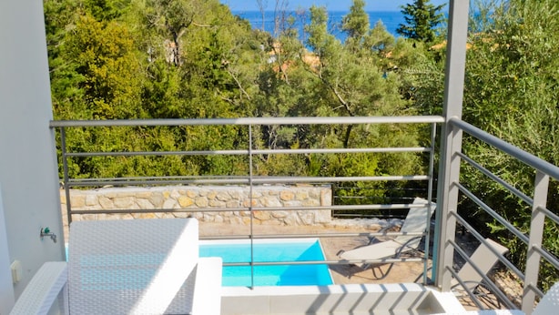 A balcony with white wicker furniture, a small pool, and a view of the sea and greenery.