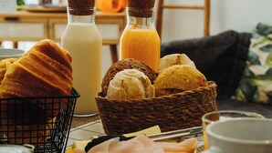 A breakfast setting with bread, pastries, a milk bottle, orange juice, and a mug on a table. - Estação do Parque (Santa Maria da Feira)