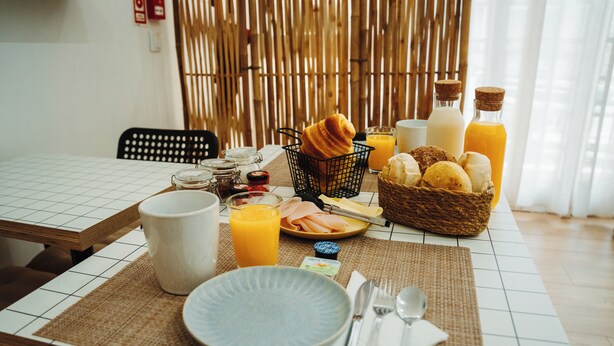 A breakfast setting with a table set for two, including plates, cutlery, a basket of bread, a bottle of orange juice, and a glass of milk. - Estação do Parque (Santa Maria da Feira)