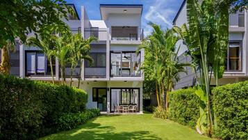 Una casa moderna de dos pisos con césped cuidado, área de estar al aire libre y exuberante vegetación tropical.