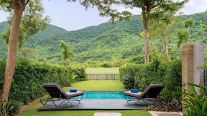 A pool area with two lounge chairs, a stone pathway, and a view of a lush green landscape with a wooden fence. - Laguna Parkside Lăng Cô (Hue)