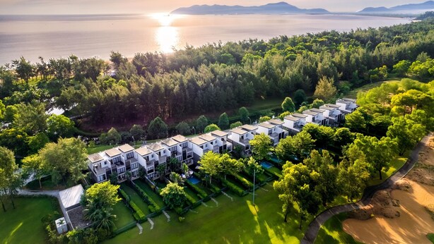 An aerial view of a modern hotel with multiple-story buildings, surrounded by lush greenery and a body of water in the background. - Laguna Parkside Lăng Cô (Hue)