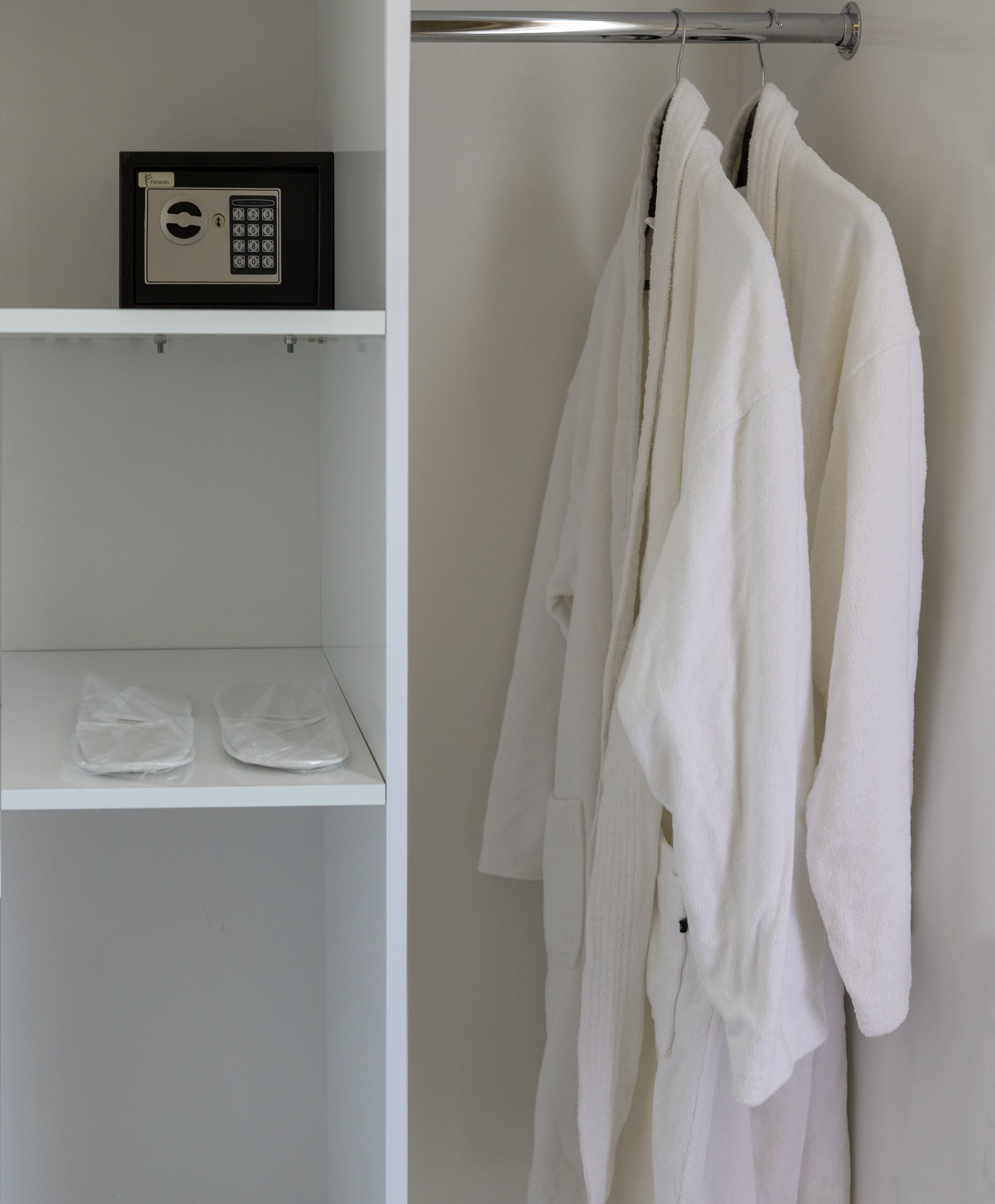 Une salle de bain avec un porte-serviettes sur lequel sont posées deux serviettes blanches, une étagère sur laquelle se trouve un appareil noir et argenté, et une paire de sacs en plastique.