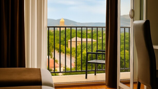 A balcony with a view of greenery and mountains, a chair, and a sofa. - Hotel Grand Palace Tbilisi (Tbilisi)