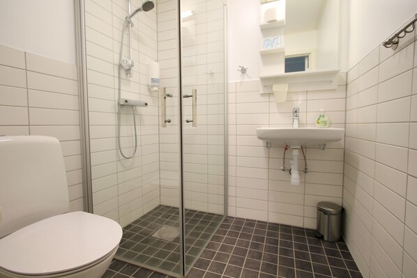 Un baño con ducha de vidrio, inodoro blanco, lavamanos y un cubo de basura.
