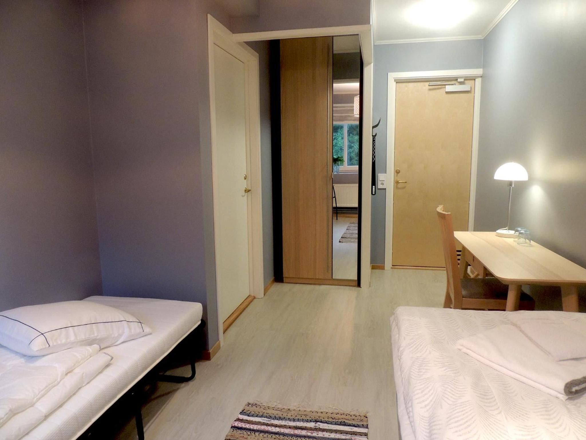 Quarto com duas camas de solteiro, uma escrivaninha de madeira e uma cadeira.