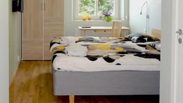 Un dormitorio con cama, escritorio, silla, armario y ventana con vista a árboles.