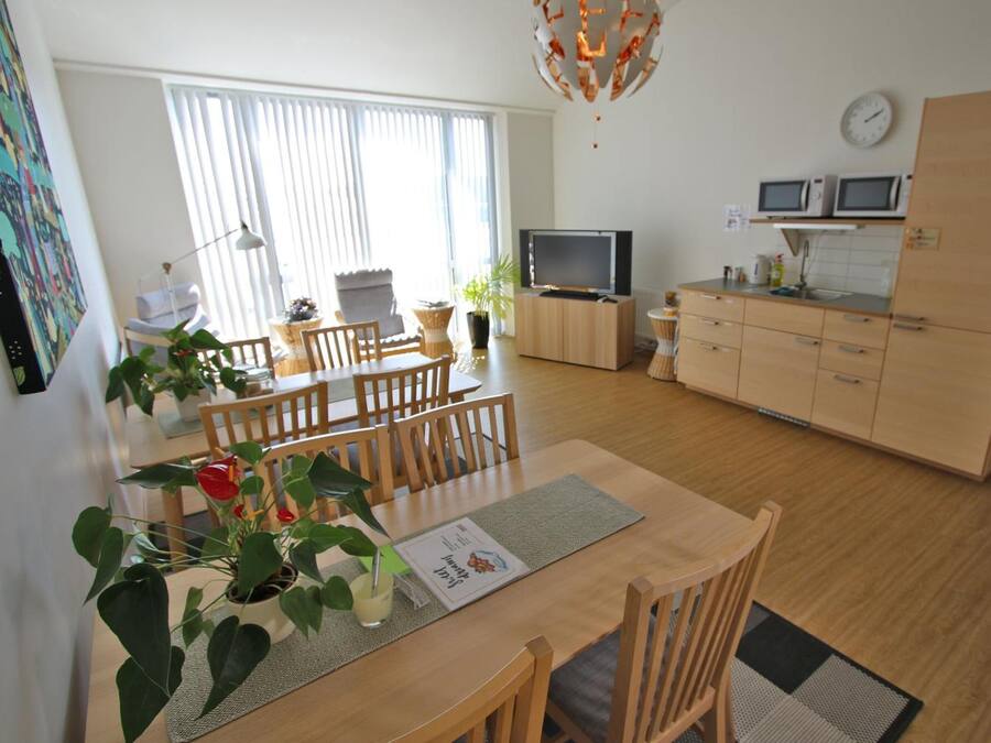 A modern kitchen with wooden cabinets, a dining area with a table and chairs, and a television on a stand.