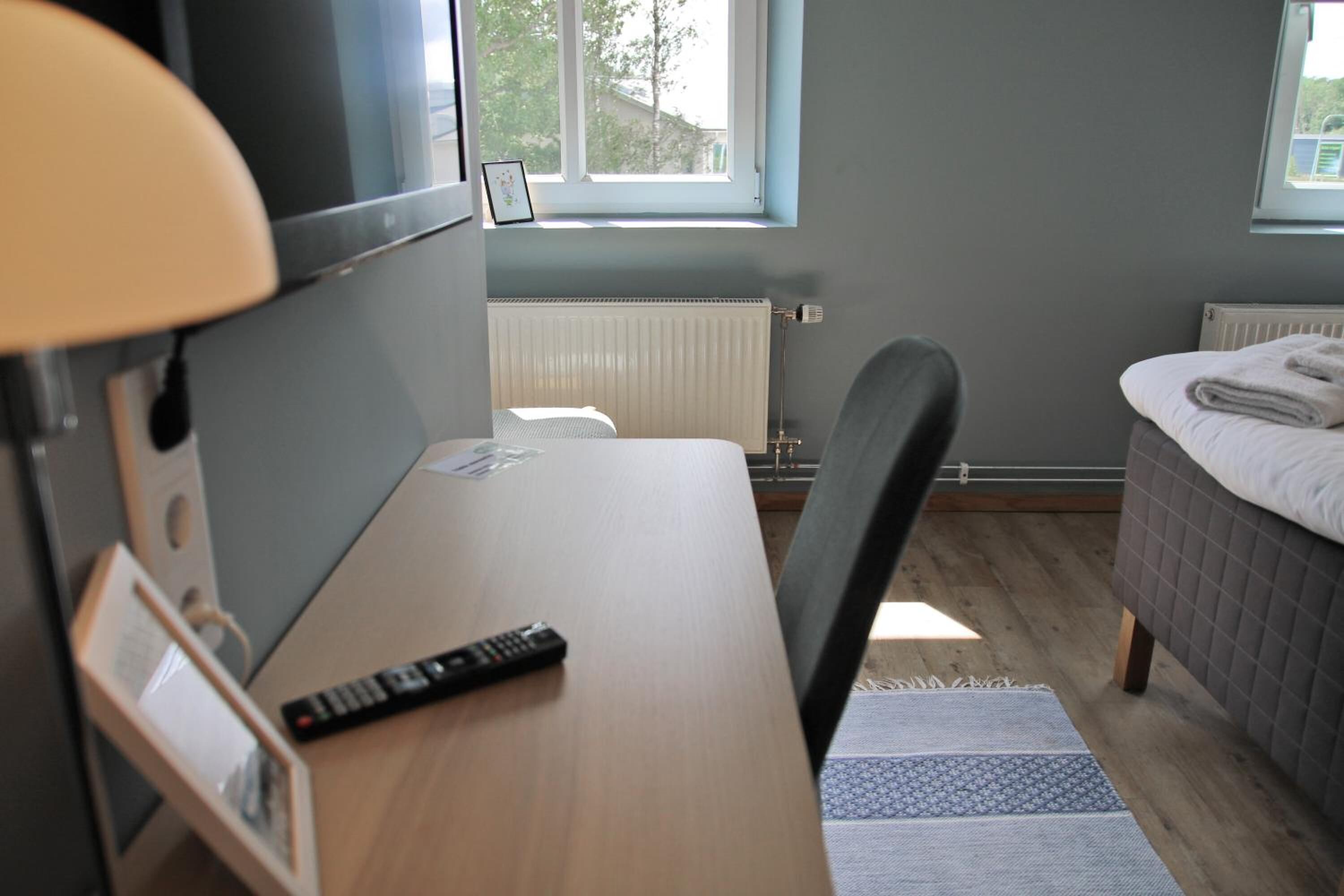 A hotel room with a bed, a desk with a chair, a window, and a radiator.