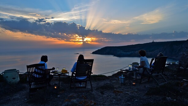 A sunset view with a table and chairs set up on a rocky shore. - Poecylia Resort (Carloforte)