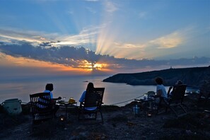 A sunset view with a table and chairs set up on a rocky shore. - Poecylia Resort (Carloforte)