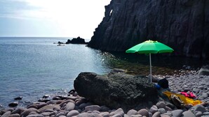 A rocky beach with a green umbrella and a person lying on a towel. - Poecylia Resort (Carloforte)