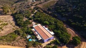 An aerial view of a property with a large building, surrounded by greenery and a coastal backdrop. - Poecylia Resort (Carloforte)