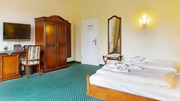 A hotel room with a bed, a desk with a chair, a wardrobe, a television, and a mirror.