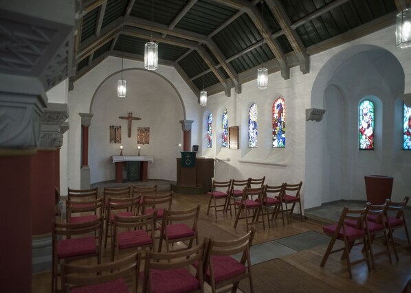 Interior de iglesia con bancas, púlpito y vidrieras de colores.