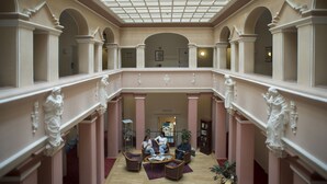 Um hall amplo com teto alto, colunas ornamentadas e uma área de estar central com mesas e cadeiras.