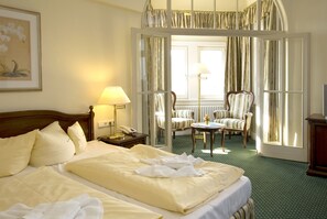 A hotel room with a large bed, a sitting area with chairs, a table, and a view through a glass door. - Hotel Haus Hainstein (Eisenach)