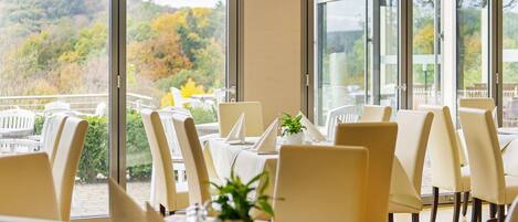 A restaurant with tables set for dining, large windows offering a view of a forested landscape.