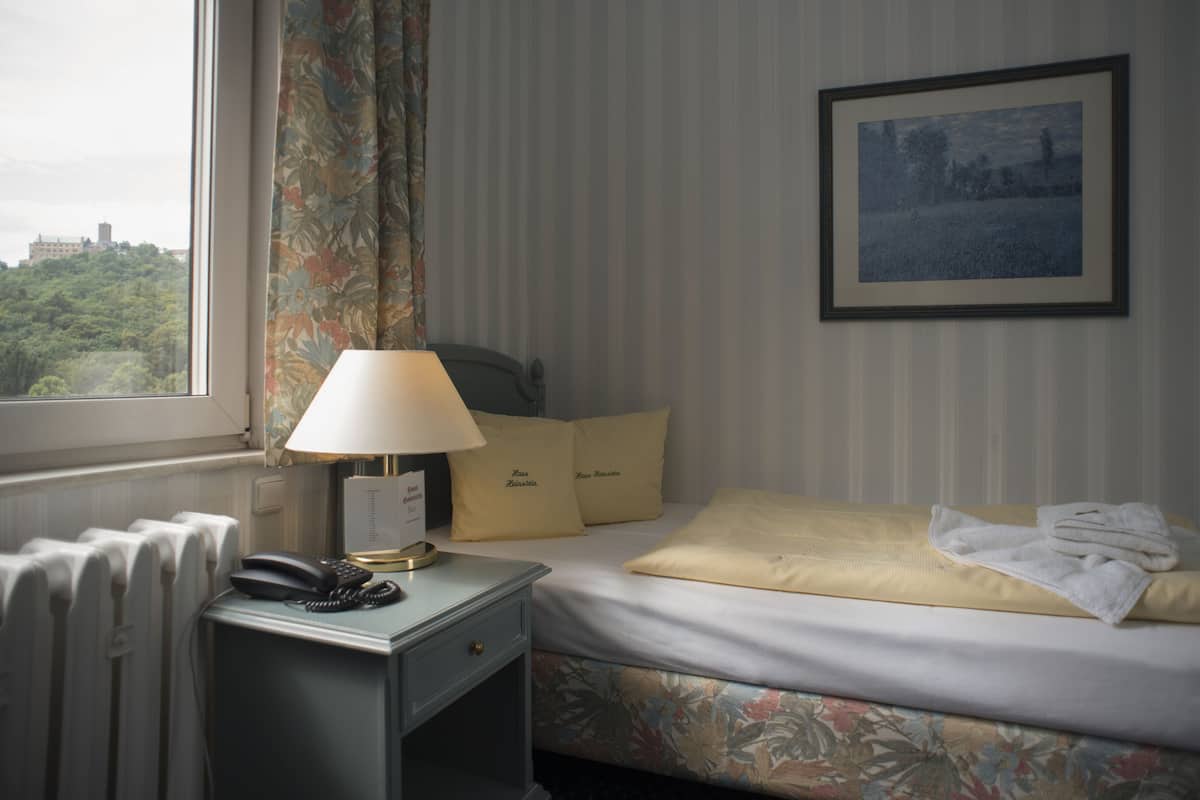 Een hotelkamer met een bed, een nachtkastje met een lamp, een telefoon en een lijst in een fotokader aan de muur.