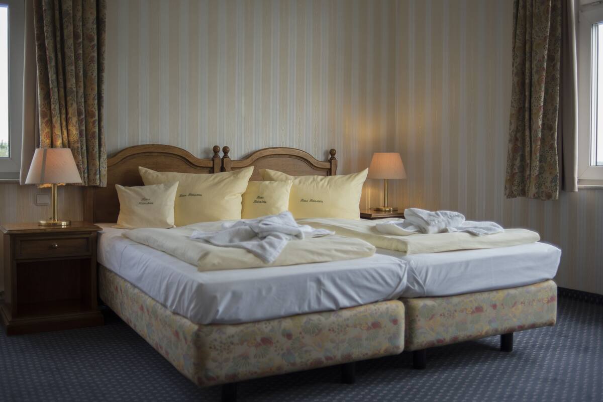 Een hotelkamer met een tweepersoonsbed, twee nachtkastjes en een raam met gordijnen.