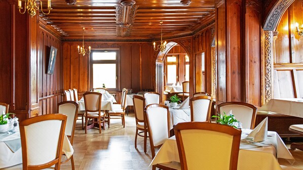A restaurant with wooden paneling, chandeliers, and white tablecloths. - Hotel Haus Hainstein (Eisenach)