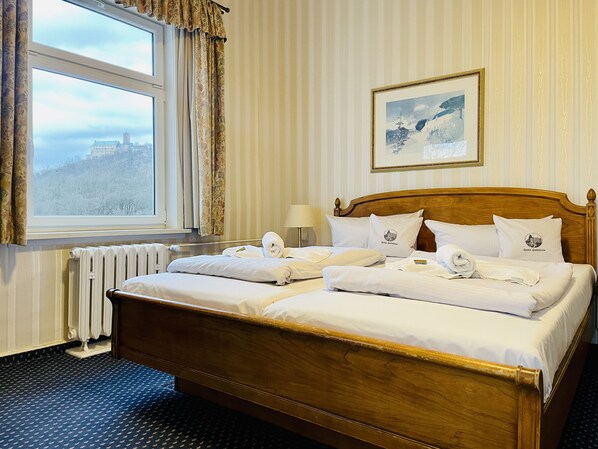 Habitación de hotel con una cama grande, una ventana con cortinas, un radiador, un cuadro en la pared y una lámpara en la mesita de noche.