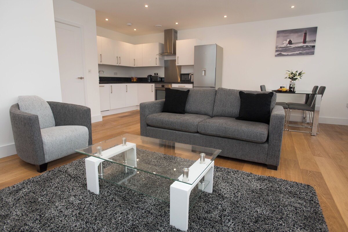 Ein modernes Wohnzimmer mit einem grauen Sofa, einem Glastisch und einem Essbereich mit Tisch und Stühlen.