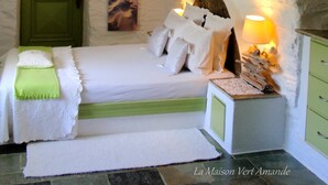 A cozy bedroom with a stone ceiling, a green door, a bed with white linens, and a night sky painting on the wall. - La Maison Vert Amande (Kea)