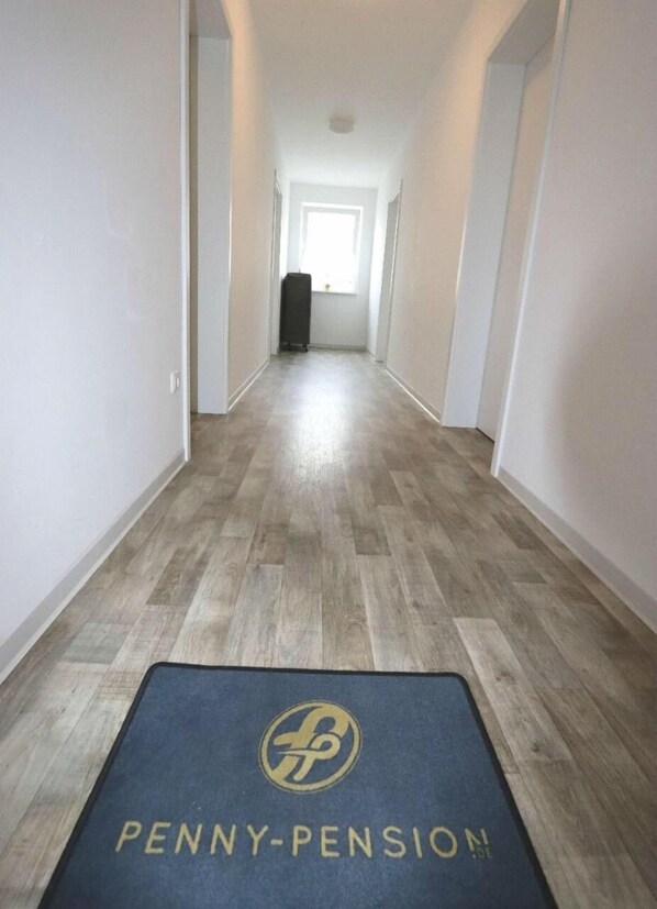 A hallway with a wooden floor and a blue mat with "PENNY-PENSION" text.