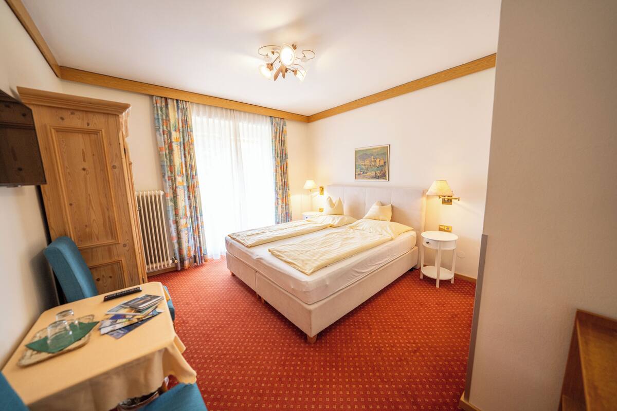 Ein Hotelzimmer mit Bett, Tisch, Stuhl, Nachttisch, Deckenventilator und Heizkörper.