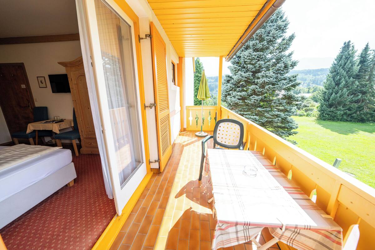 Ein Zimmer mit einem Bett, einem Tisch mit Stühlen und einem Balkon mit Blick auf Bäume und eine Wiese.