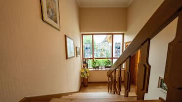 A wooden staircase with a handrail leading to a landing. There are framed pictures on the walls and a window with a view of greenery outside.