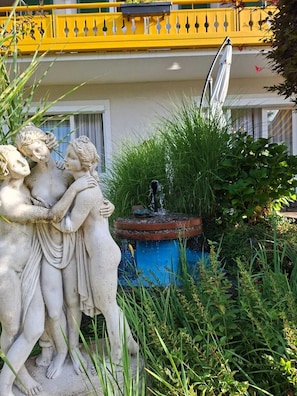 Un jardín con una estatua de tres figuras, una fuente y una barandilla amarilla.