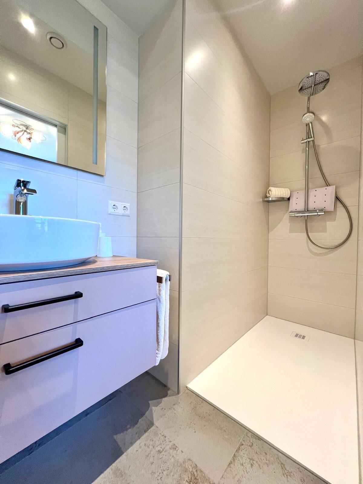 A modern bathroom with a white vanity, a mirror, and a shower with a handheld showerhead.