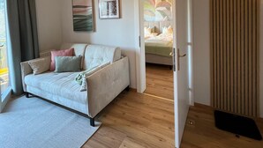 Una sala de estar moderna con un sofá, un tapete y piso de madera. Hay una puerta que da a otra habitación.