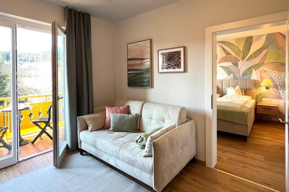 Ein modernes Wohnzimmer mit einer Couch, einem Couchtisch und einem großen Fenster. Durch das Fenster ist ein Balkon zu sehen.