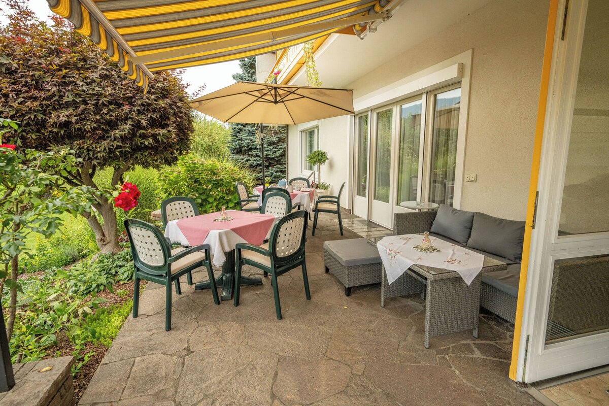 An outdoor patio with a table and chairs, a covered seating area, and a view of the garden.