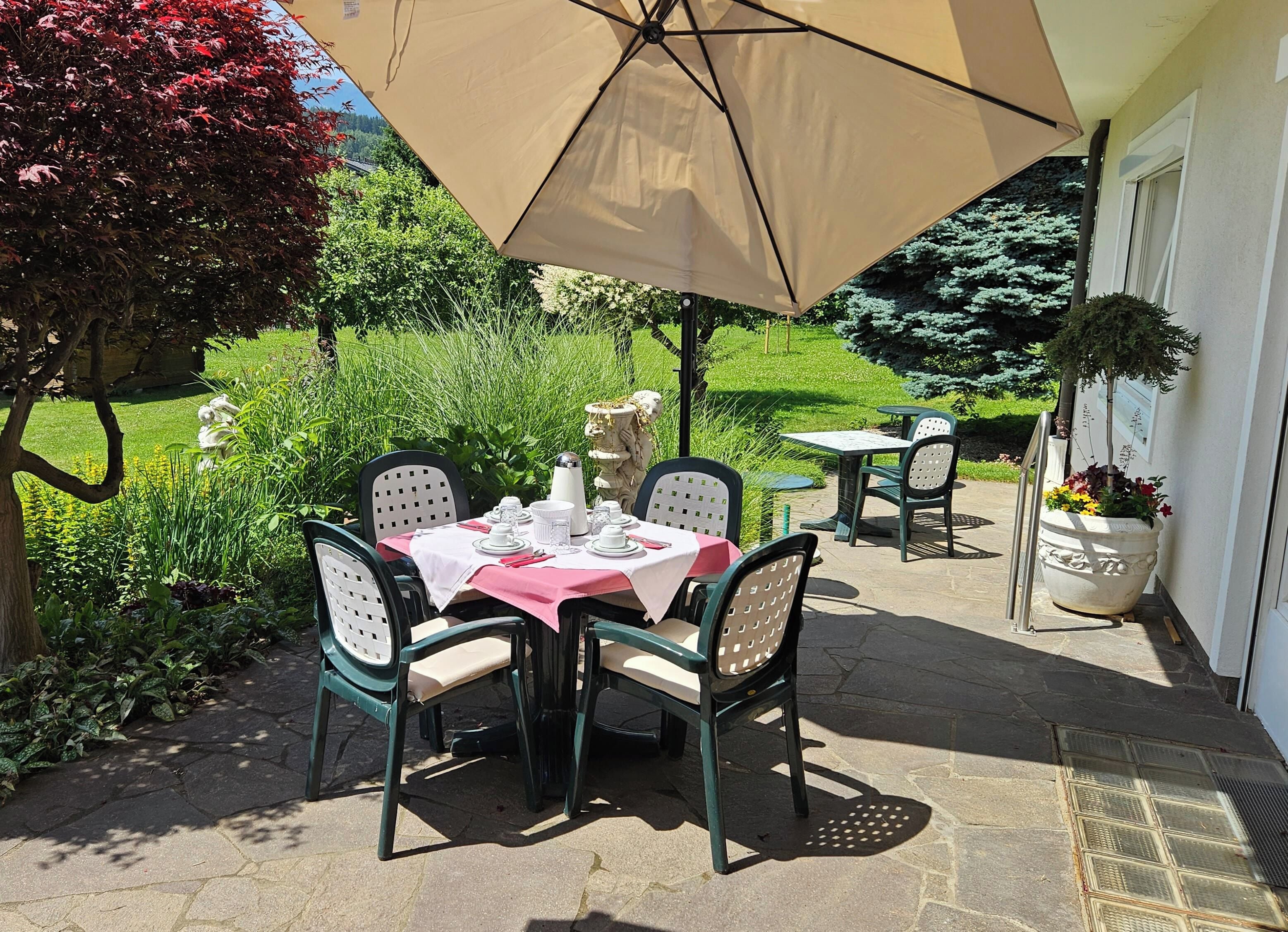 Un patio exterior con una mesa lista para comer, rodeada de sillas y una sombrilla que da sombra.