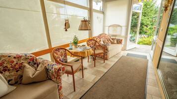 A sunlit room with a sofa, chairs, a small table, and a view of a garden through a glass door.